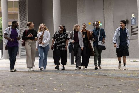 Diverse office team walking through urban plaza laughing, carrying coffee and backpacks