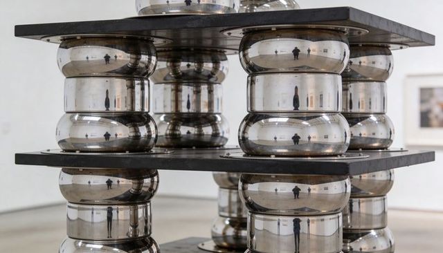 Stacked chrome sculpture reflecting gallery visitors in minimalist contemporary interior