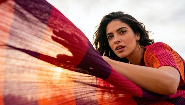 Young woman leaning and stretching colorful sheer scarf backlit by sunset light