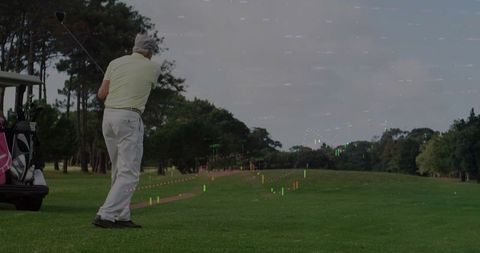 Senior golfer swinging on fairway with golf cart and digital trajectory analytics overlay