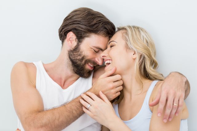 This image depicts a romantic couple embracing and laughing in a bedroom, showcasing love and intimacy. Ideal for use in relationship blogs, lifestyle articles, and advertisements promoting romance, home life, or couple's products.