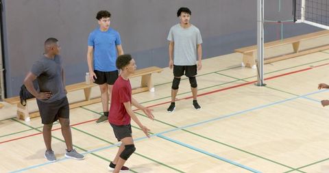 Diverse male volleyball team practicing indoor court receiving drill with knee pads and teamwork