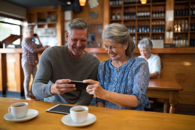 Happy senior couple looking their photos on mobile phone in restaurant
