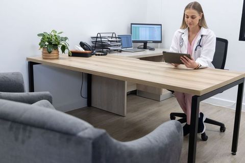 Female doctor reviewing tablet in modern clinic office with desktop monitor and plant