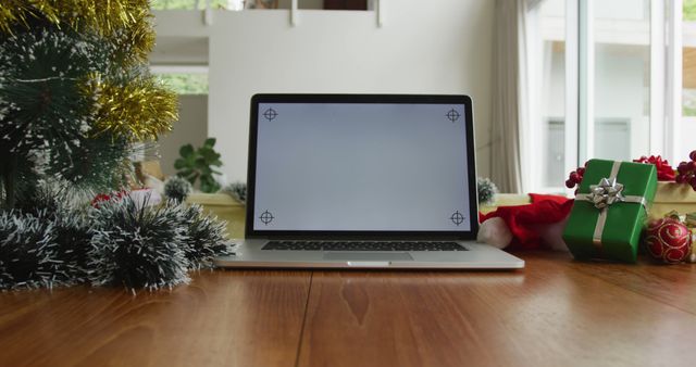 Bright setup featuring open laptop surrounded by Christmas decorations on wooden table. Perfect for holiday-themed projects, remote work during holidays, online shopping concepts, and festive backgrounds.