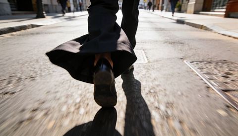 Commuter walking away on sunlit urban street with scuffed leather shoe and trousers