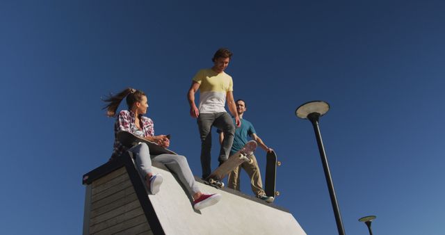 Happy caucasian woman and two male friends skateboarding on sunny day. hanging out at skate park in summer.