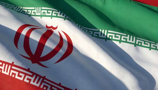 Sunlit iranian flag waving closeup showing red emblem and kufic border