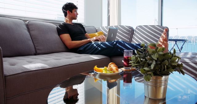 Young Man Relaxing on Sofa with Laptop in Bright Modern Living Room - Download Free Stock Images Pikwizard.com