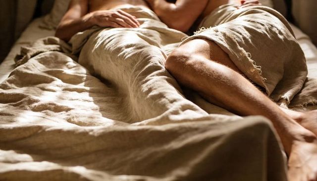 Sunlit linen bed couple reclining intimate cozy morning with bare leg detail
