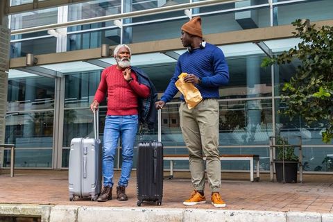 Multigenerational travelers standing with suitcases outside modern glass transport terminal