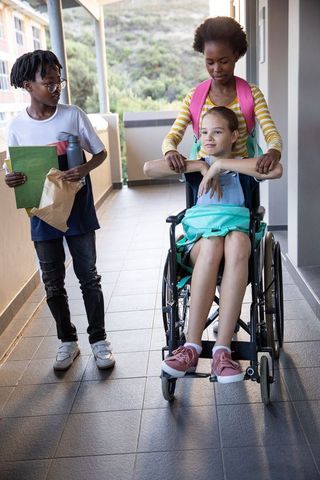 Classmates supportively pushing wheelchair in school hallway