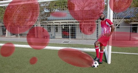 Confident male soccer player posing at goalpost with foot on ball on artificial turf
