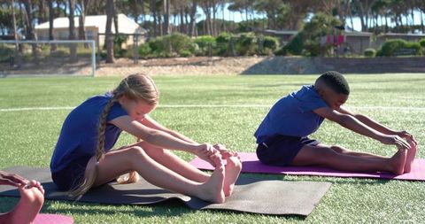 Children stretching on soccer turf during outdoor school fitness and yoga class promoting teamwork