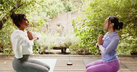 Two women meditating on yoga mats in tranquil outdoor setting