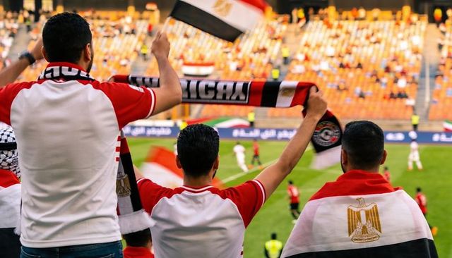 Egyptian football fans cheering in stadium holding scarves and draped national flags