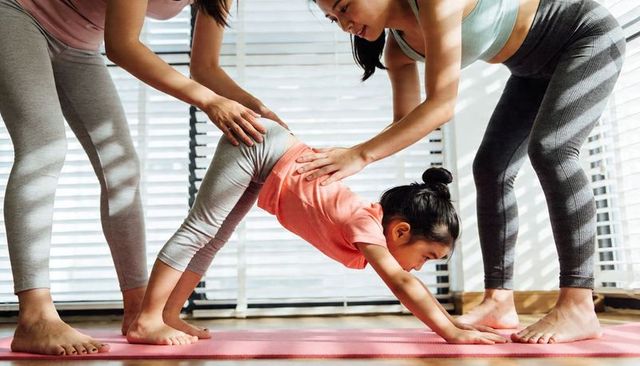 Child practicing downward dog while instructors guiding on home yoga mat in sunlit room