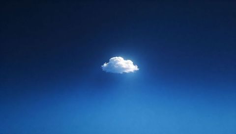 Drifting single cumulus cloud glowing with sunlit rim over deep indigo gradient sky