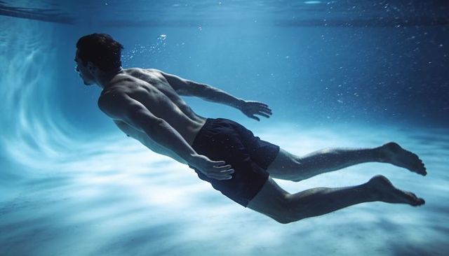Male swimmer gliding underwater in streamlined pose with caustic light and bubbles