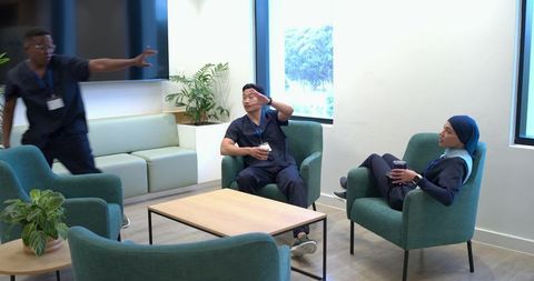 Multicultural medical staff taking coffee break and chatting in modern hospital lounge