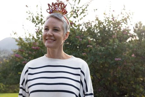Senior woman wearing merry christmas headband smiling in garden in striped sweater