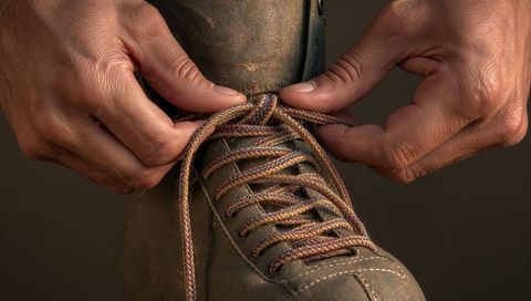 Closeup of hands tying sturdy leather boot laces, rustic workwear footwear texture
