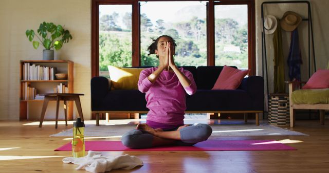 Biracial woman practicing yoga and meditating while sitting on yoga mat at home - Download Free Stock Photos Pikwizard.com