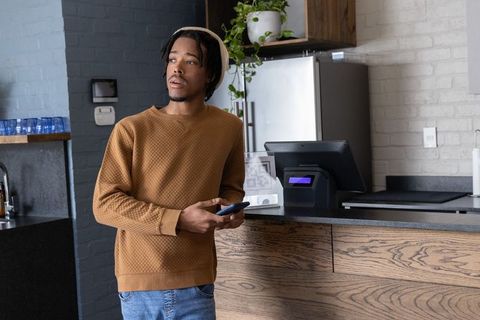 African american man standing at cafe counter holding smartphone using contactless payment