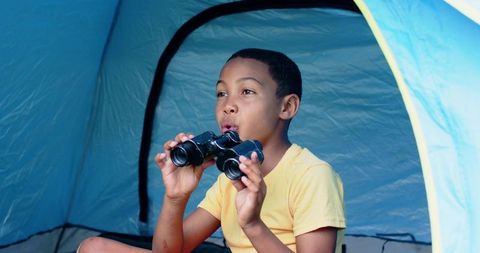 Curious african boy camping with binoculars in blue tent exploring nature and adventure