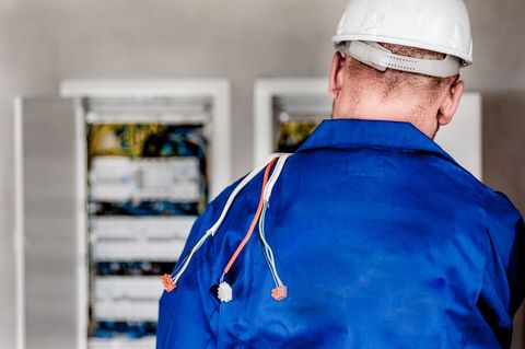 Electrician in blue coat wiring electrical panel