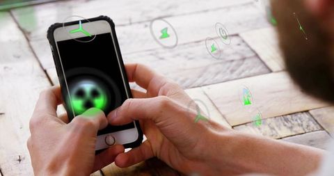 Hands tapping smartphone with green holographic icons on wooden table, futuristic ui