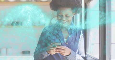 Smiling woman using smartphone by window with turquoise augmented reality data overlay