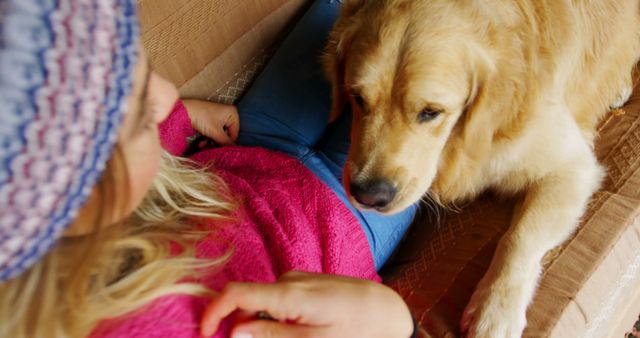 Young girl in casual wear cuddling with her golden retriever on sofa. Ideal for use in advertising related to pets, family life, and emotional bonding. Useful for portrayals of indoor activities and highlighting the connection between children and pets.