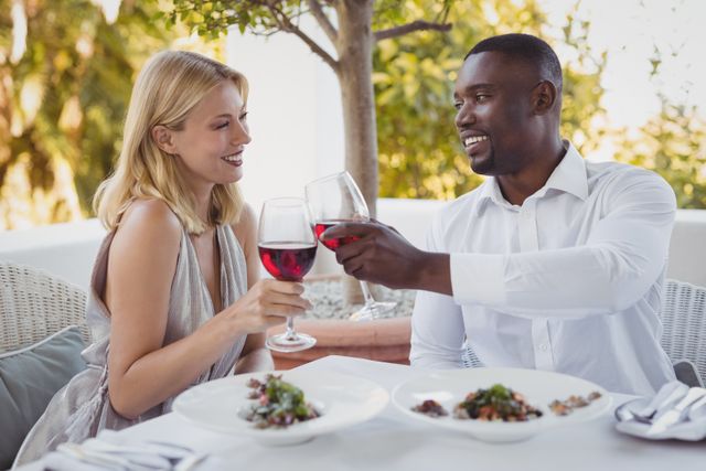 Romantic couple toasting wine glasses while dining in an elegant outdoor restaurant. Ideal for use in advertisements for restaurants, romantic getaways, lifestyle blogs, and relationship advice articles.