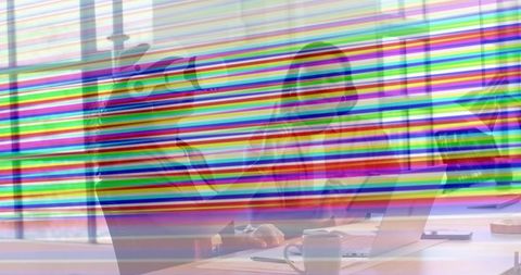 Two women collaborating at office desk with laptop and coffee, colorful scan-line distortion