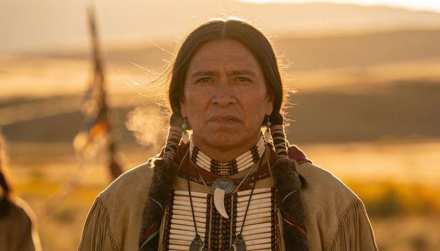 Native american elder standing in traditional regalia with beadwork and bone pendant at sunset