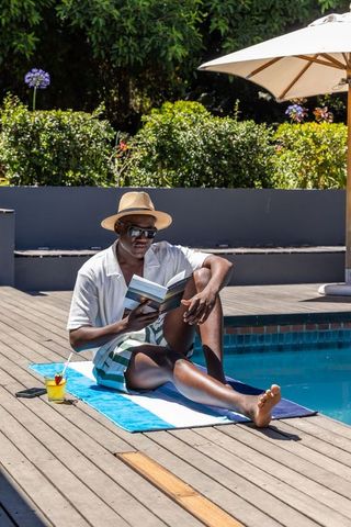 Relaxing african american man reading poolside in straw hat and sunglasses on summer day