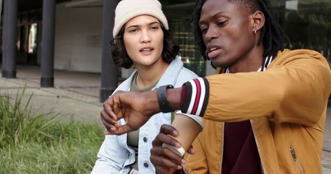 Multicultural friends checking smartwatch while holding coffee during casual outdoor chat