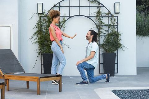 Romantic poolside proposal with african american woman standing and man kneeling by trellis