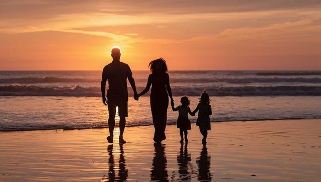 Family of Four Walking Hand in Hand on Reflective Beach at Golden Sunset Silhouette