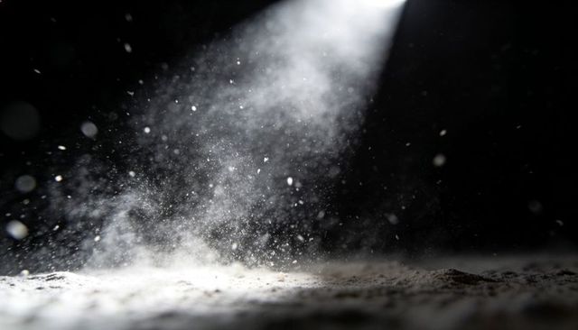Spotlight revealing floating powder particles in dark studio — dramatic light beam