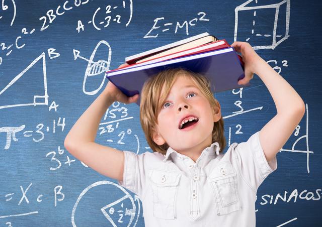 Young boy balancing books on his head in a classroom with a blackboard covered in mathematical symbols and formulas. Ideal for educational content, school promotions, learning materials, and academic websites.
