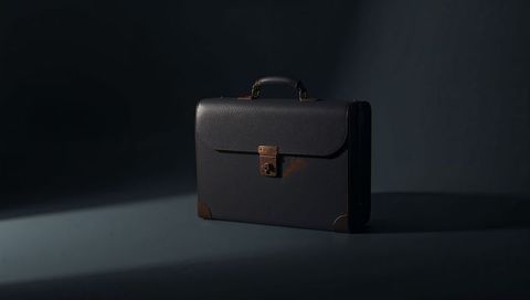 Vintage leather briefcase featuring brass latch and aged patina on dark minimal background