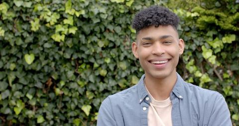 Smiling young man wearing blue shirt outdoors with ivy wall, friendly lifestyle portrait