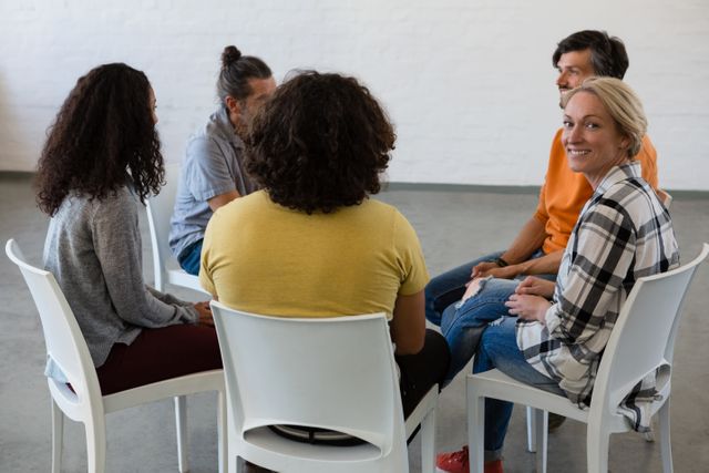 Group of people sitting in a circle, engaging in a discussion during an art class. Smiling woman looking at the camera, indicating a positive and friendly atmosphere. Ideal for illustrating teamwork, collaboration, community engagement, and educational settings.