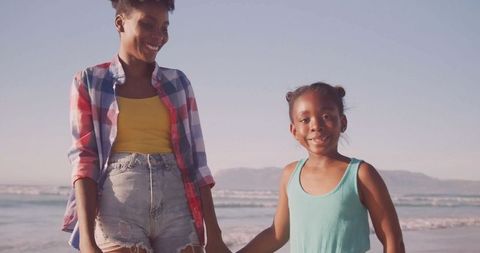 Mother and daughter walking hand in hand on beach shoreline