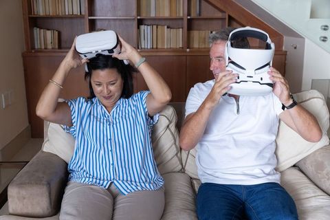 Mature couple trying virtual reality headsets on living room sofa