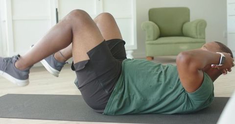 African man doing ab crunches on mat wearing smartwatch and green shirt for home workout