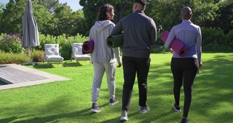 African american friends walking to outdoor yoga class carrying mats near pool