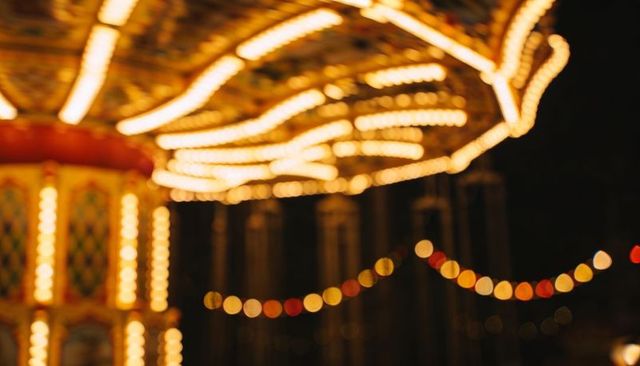 Vintage carousel canopy glowing with warm bulbs, festive bokeh and motion blur at night
